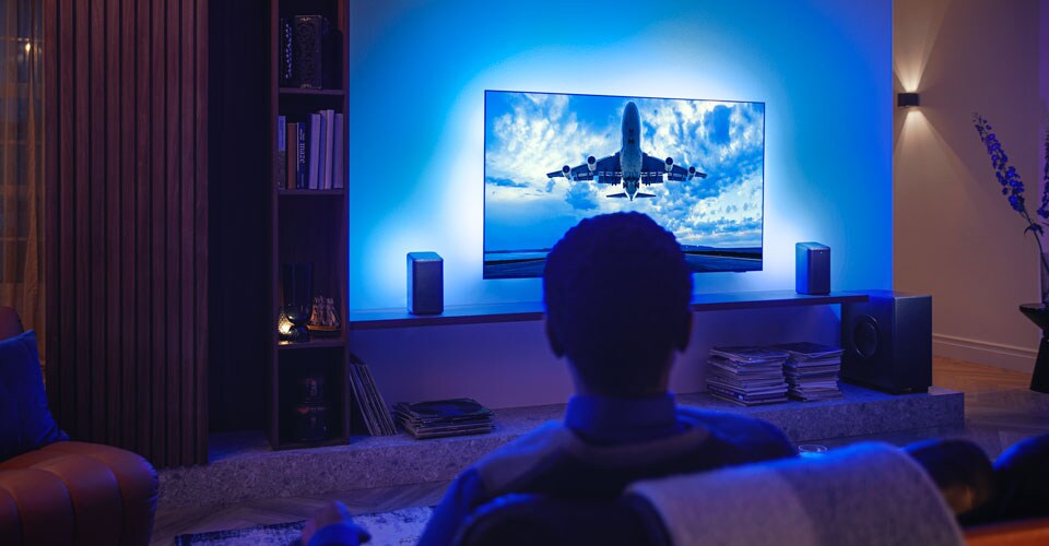 Man enjoying his Philips Ambilight tv connected to wi-fi speakers