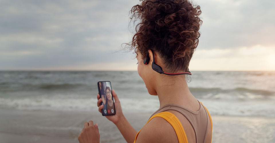Sportaš prima poziv na plaži dok koristi slušalice s prijenosom zvuka preko kosti 