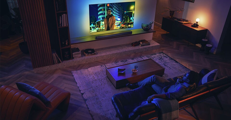 Čovjek uživa u svom Philips Ambilight TV-u sa soundbarom