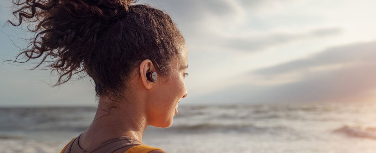 Žena upotrebljava potpuno bežične slušalice na moru