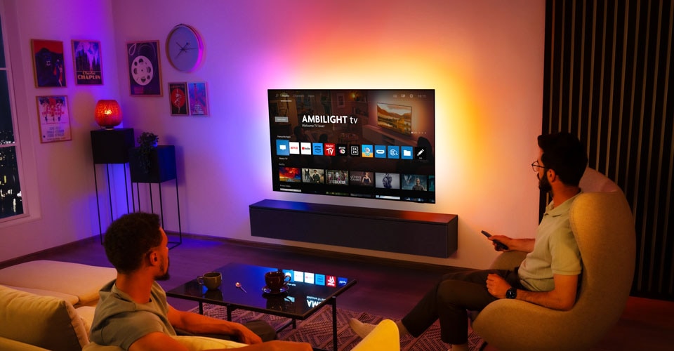 Dva muškarca gledaju Ambilight televizor postavljen na zid u dnevnoj sobi