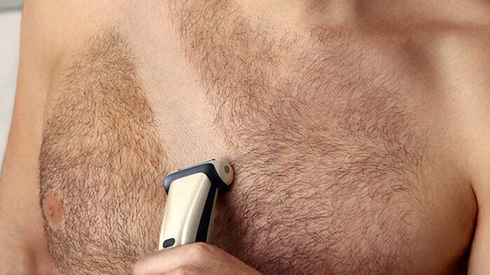 The torso of a man using a Philips Bodygroom as a body shaver to shave his chest hair.