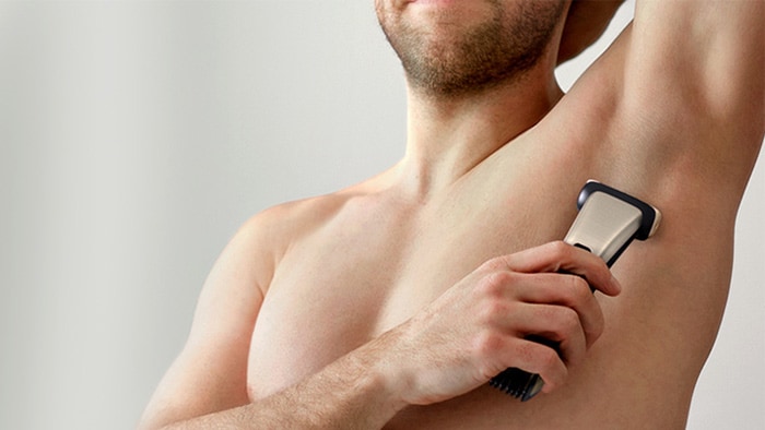 The clean-shaven torso of a man using a Philips Bodygroom body shaver to shave his underarms